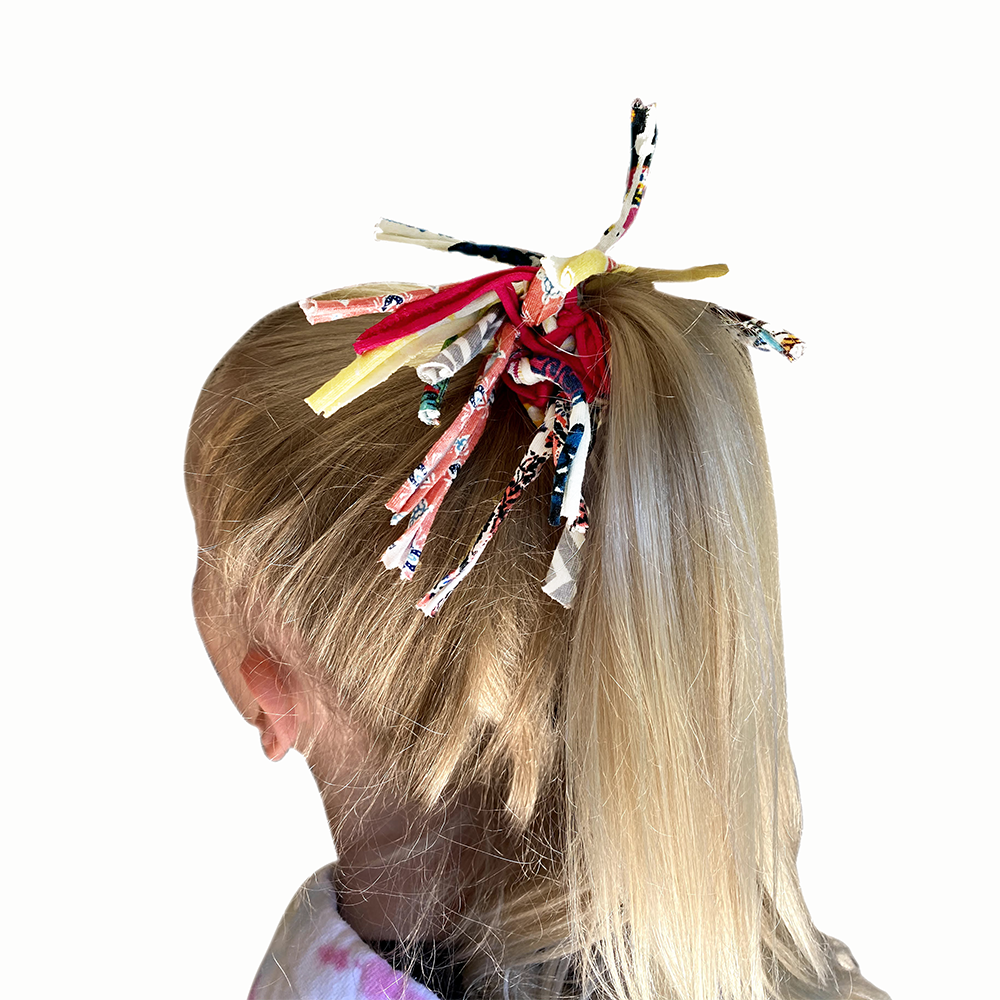Child's hair with colorful ribbons tied in a ponytail on a white background
