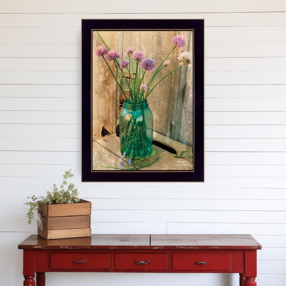 Framed artwork of a green vase with flowers on a white wall above a red table.