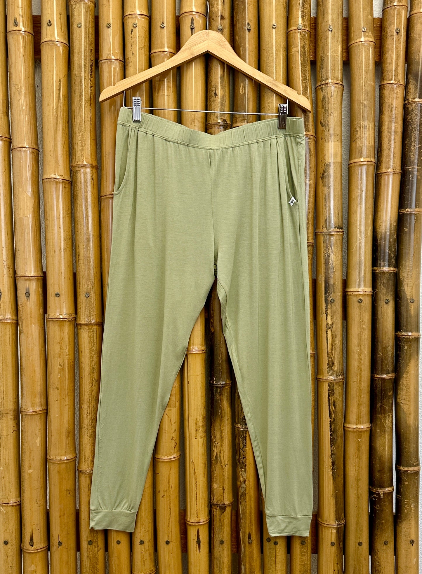 Green pants on a hanger against a bamboo wall