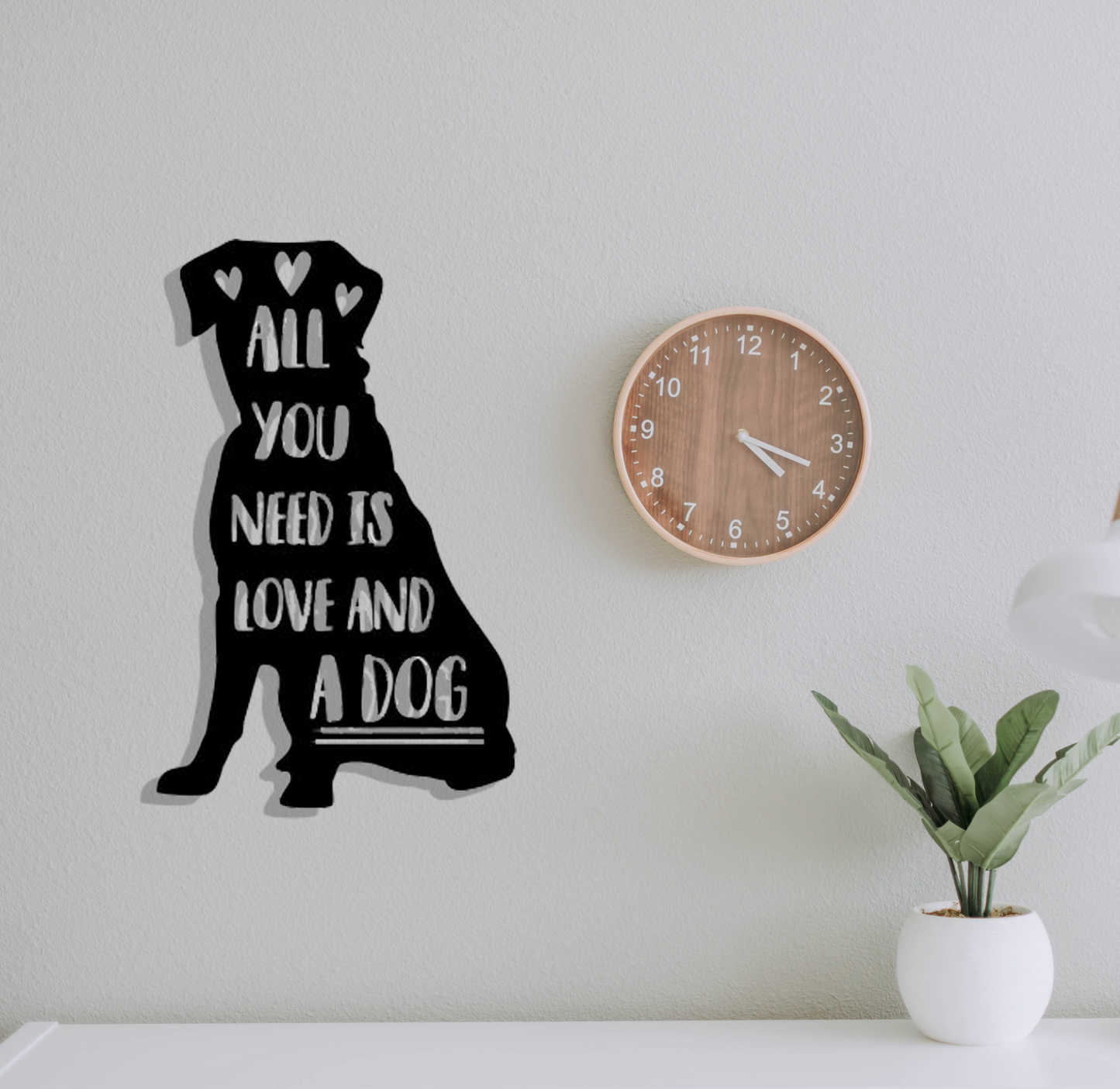 Black dog silhouette wall art with 'All you need is love and a dog' text on a light gray wall with a clock and plant.