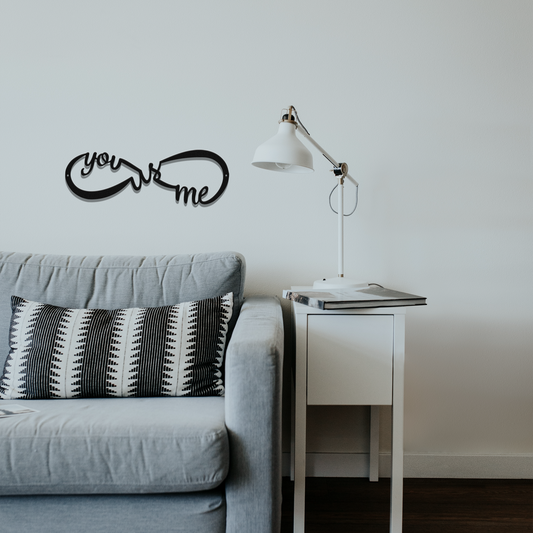 Gray sofa with a decorative pillow and 'you & me' wall art in a minimalistic living room.
