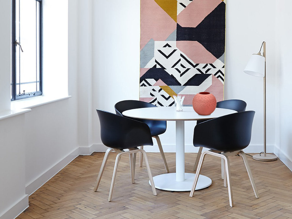 Modern dining area with a round white table and black chairs, featuring a geometric-patterned wall art piece.