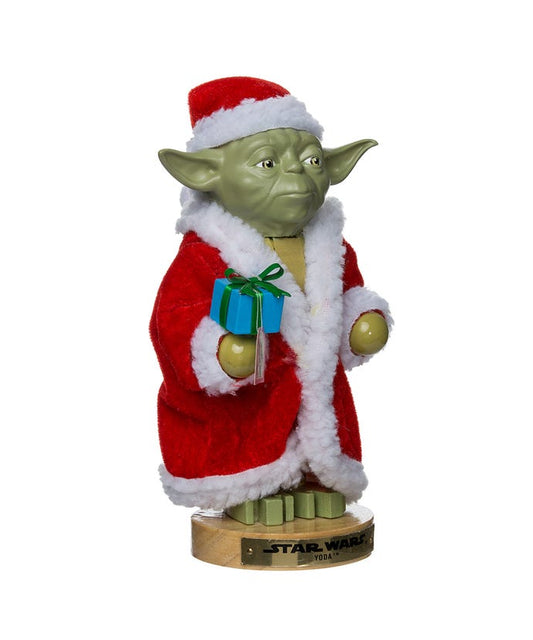 Yoda figurine dressed in a Santa Claus outfit with a gift on a white background