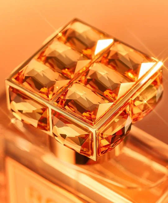 Close-up of a perfume bottle with a large, faceted crystal on an orange background