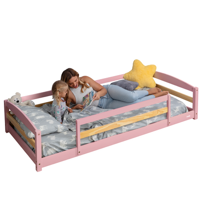 Woman and child on a pink bed with wooden sides, reading a book.