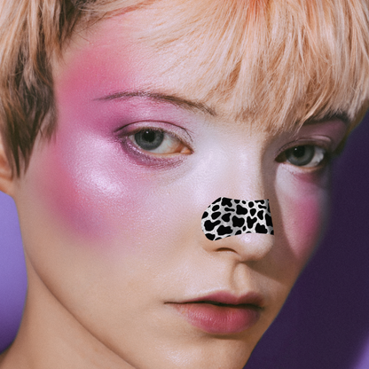 Close-up of a person with pink makeup and a leopard print sticker on their nose against a purple background