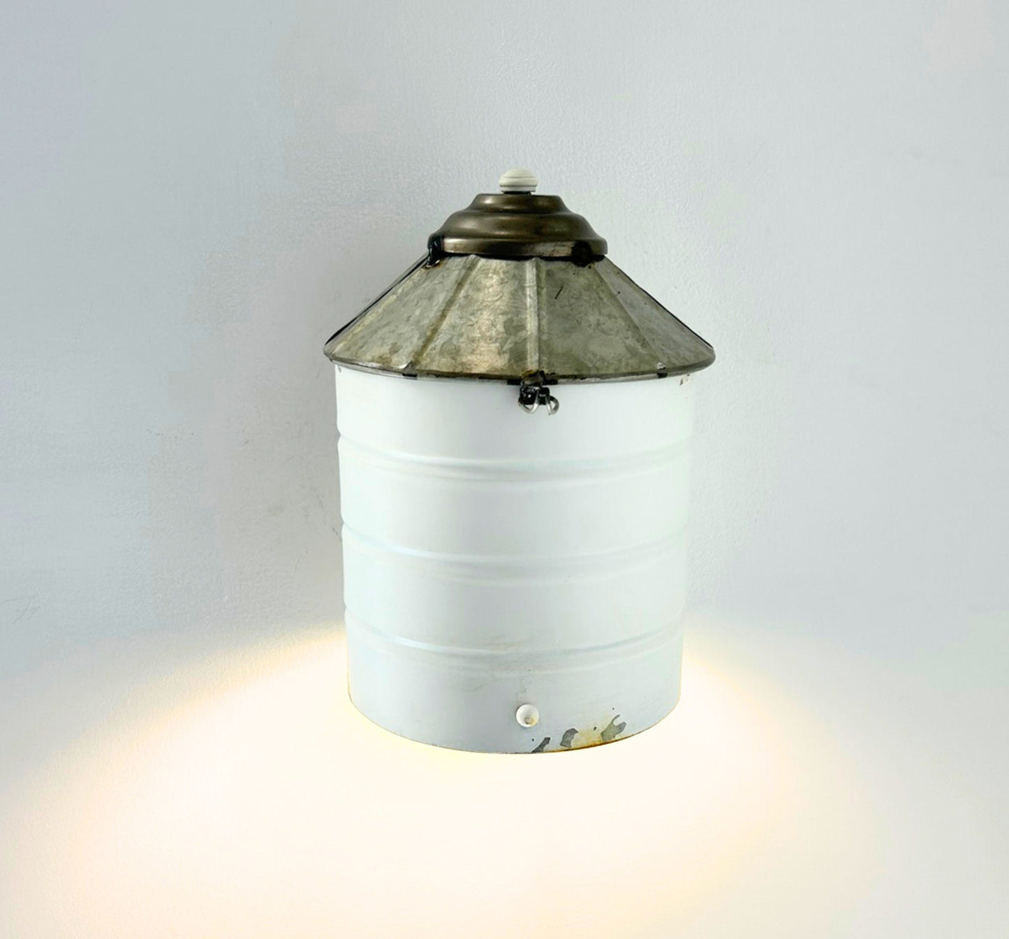 Wall-mounted light fixture with a white base and decorative metal top on a gray background