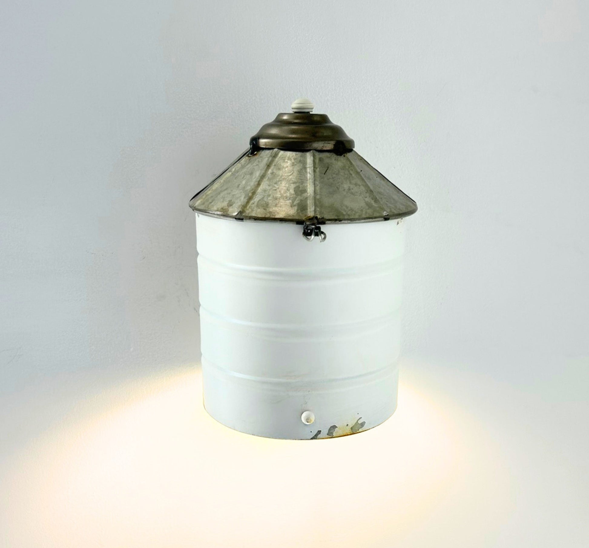 Wall-mounted light fixture with a white base and decorative metal top on a gray background