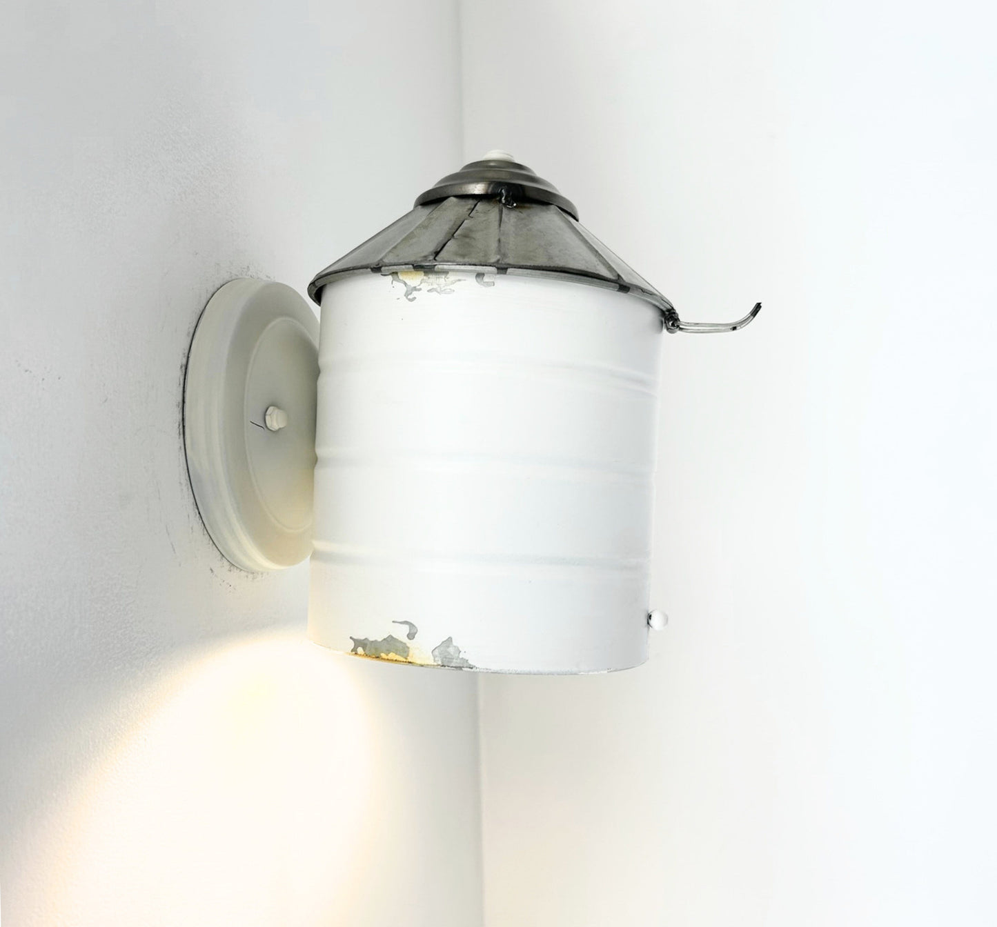 Wall-mounted light fixture with white shade and metallic top on a plain wall.