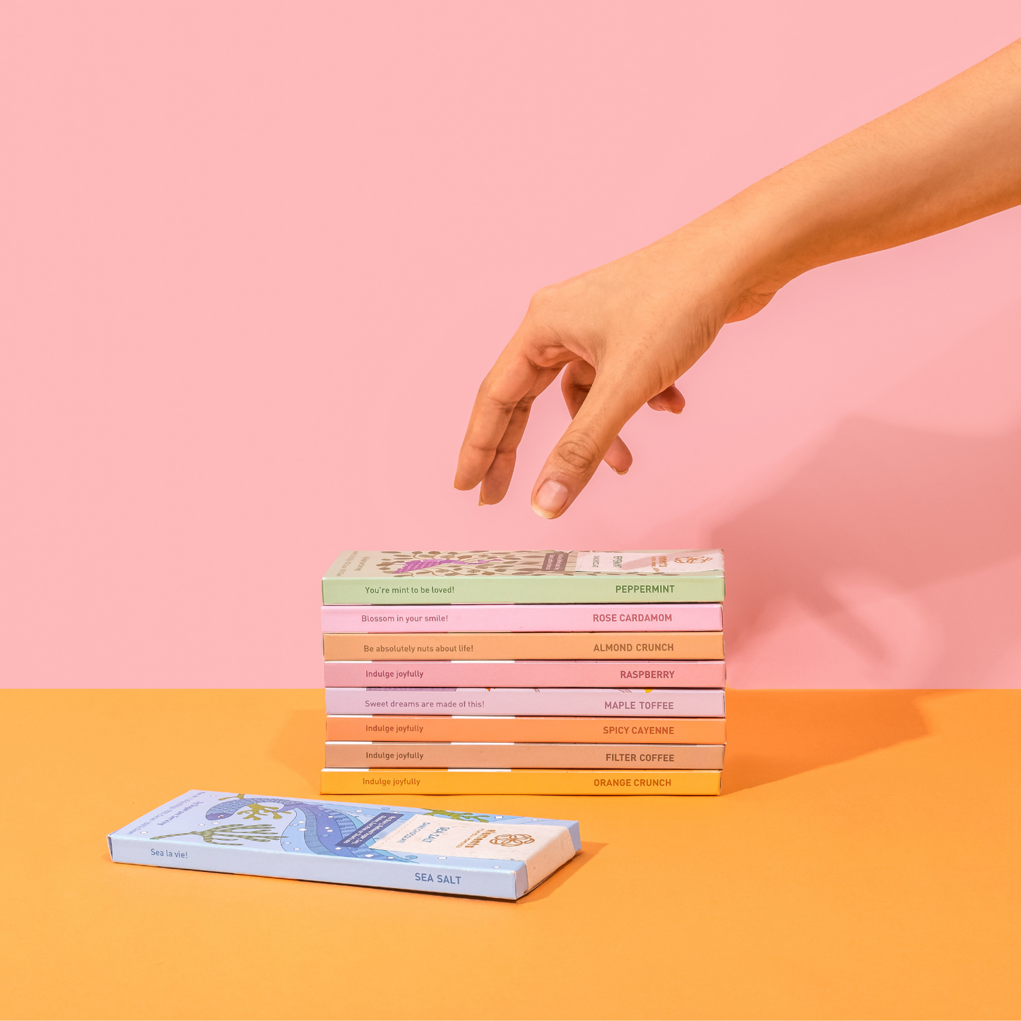 Stack of colorful boxes on a pink and orange background with a hand reaching towards them.