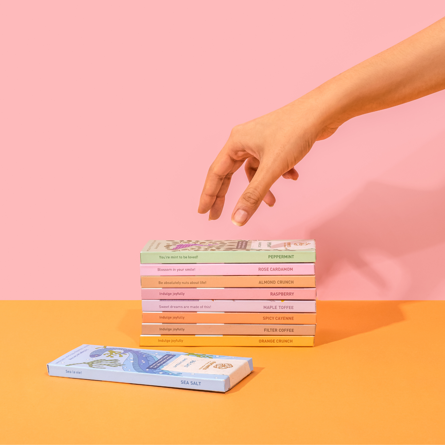 Stack of colorful boxes on a pink and orange background with a hand reaching towards them.