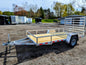Metal utility trailer with wooden floor on a dirt lot with trees in the background