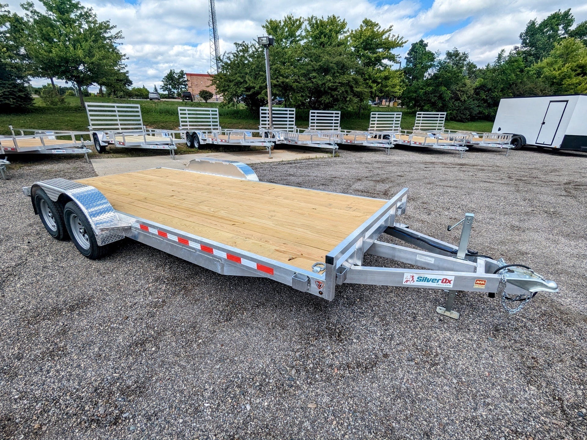 Car trailer with a wooden floor in a parking lot with other trailers in the background.