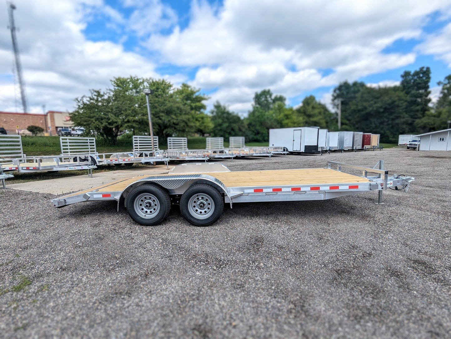 Flatbed trailer parked on a gravel lot with trees and buildings in the background