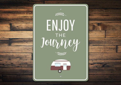 Decorative sign with 'Enjoy the Journey' text and a camper illustration on a wooden background