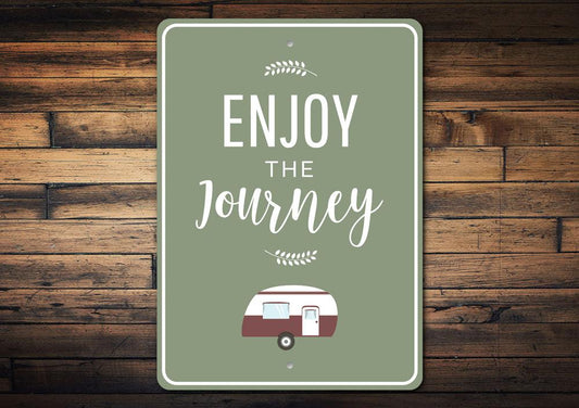 Decorative sign with 'Enjoy the Journey' text and a camper illustration on a wooden background