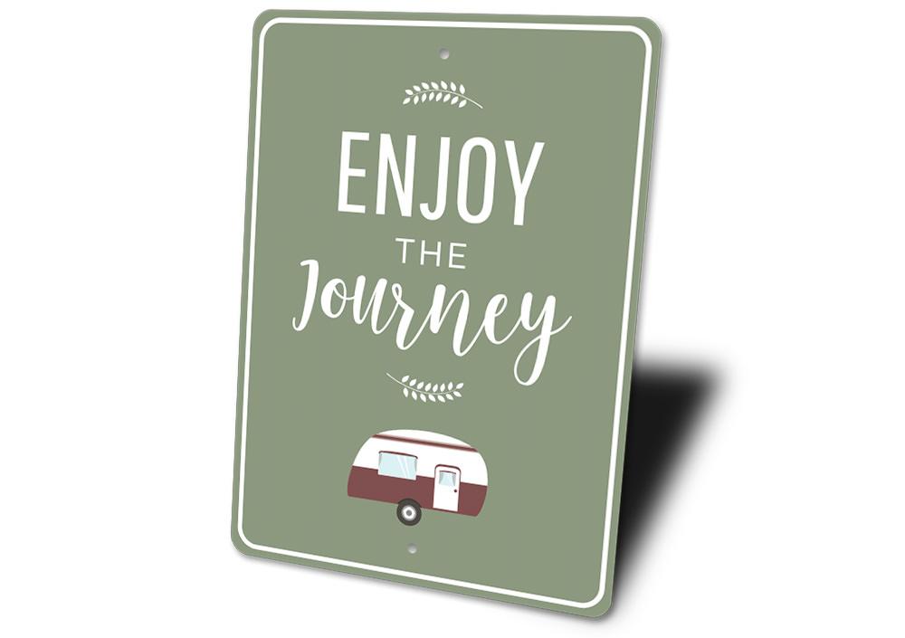 Green sign with 'Enjoy the Journey' text and a small camper illustration on a white background