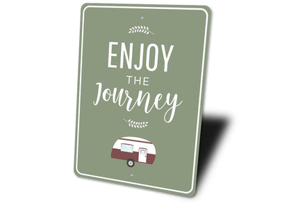 Green sign with 'Enjoy the Journey' text and a small camper illustration on a white background