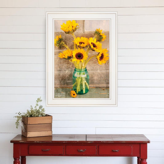 Framed artwork of sunflowers in a vase on a white wall above a red wooden table.