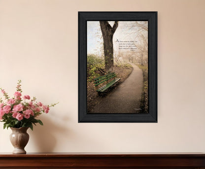 Framed print of a park scene with a bench and tree, placed on a wall above a vase with flowers.