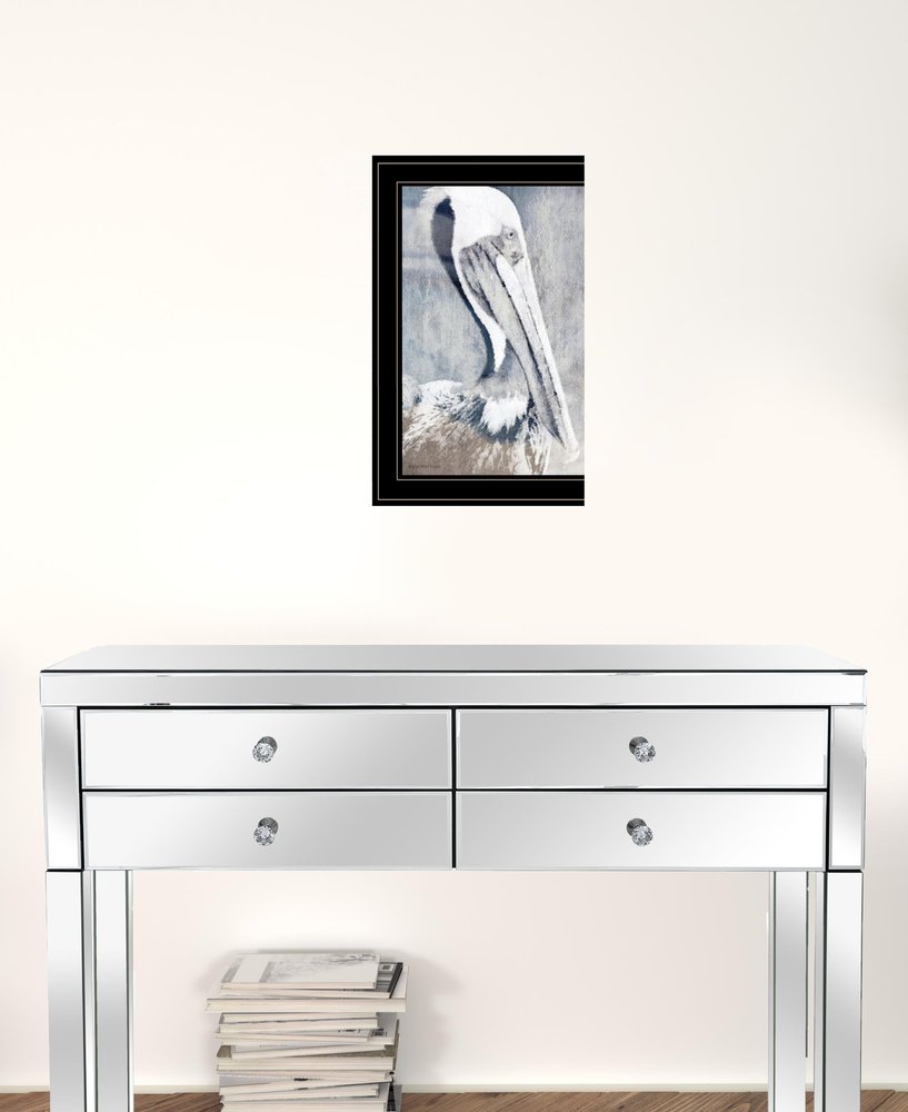 Framed artwork of a pelican above a mirrored console table with books on a white wall.