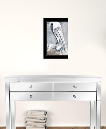 Framed artwork of a pelican above a mirrored console table with books on a white wall.