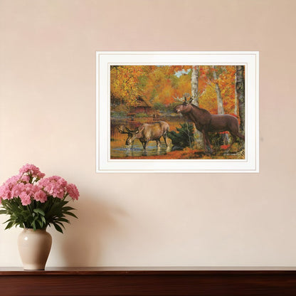 Framed painting of two moose in a forest scene on a wall above a vase with pink flowers.