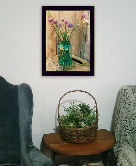 Framed picture of a vase with flowers on a wall above a table with a basket of plants.