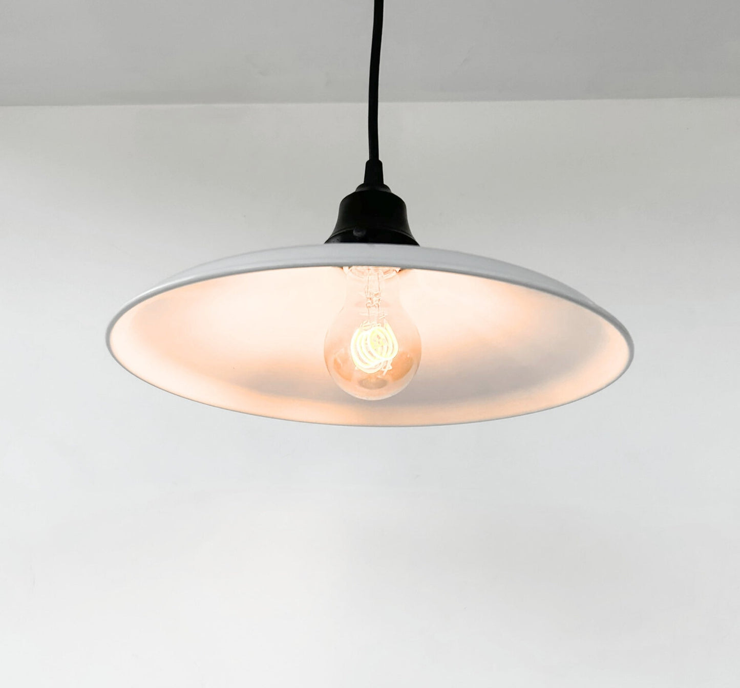 Pendant light with a white shade and black cord on a plain background