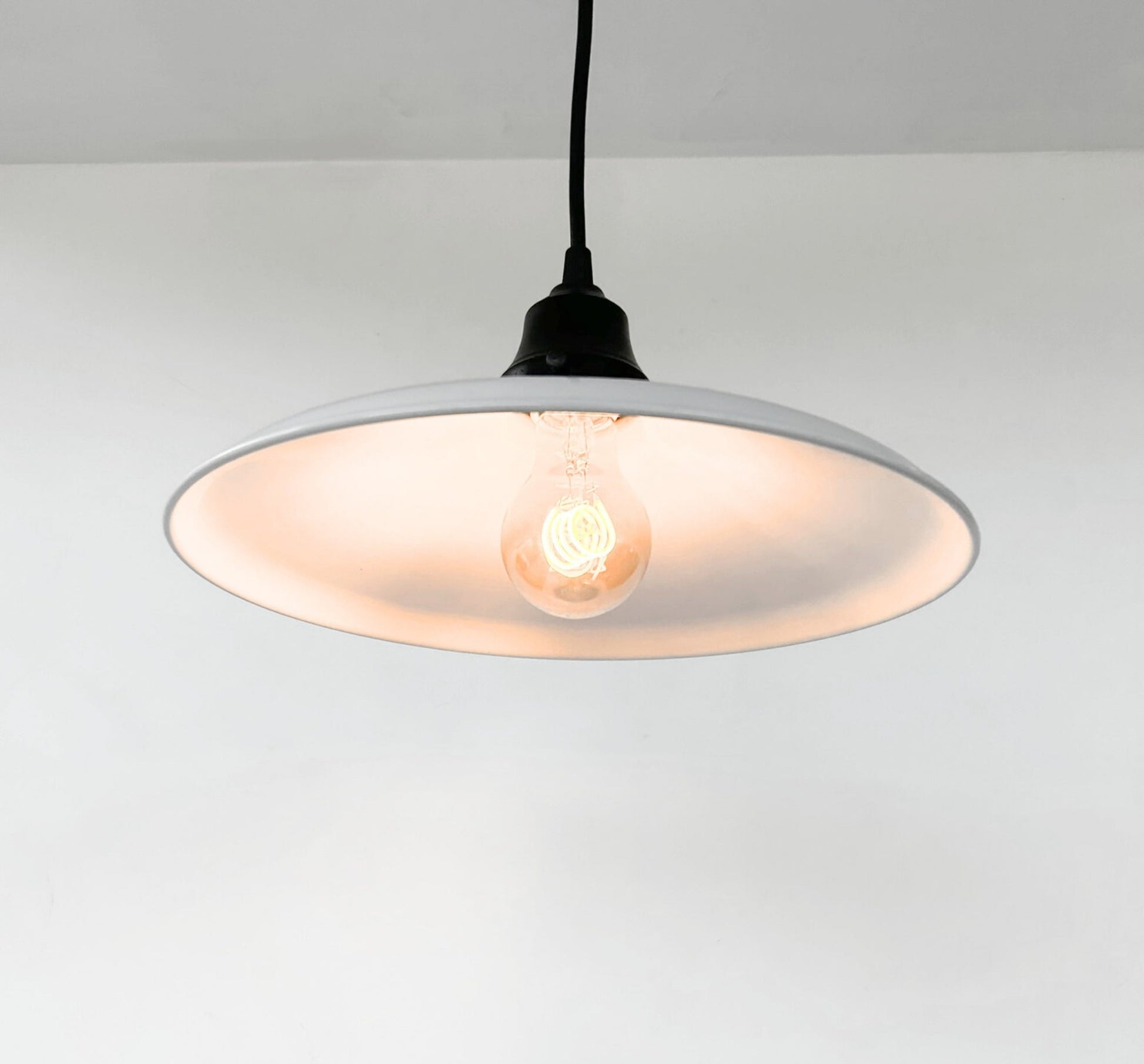 Pendant light with a white shade and black cord on a plain background