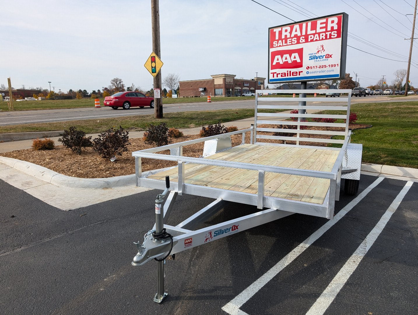 White utility trailer on a paved road with a 'Trailer Sales & Parts' sign in the background.