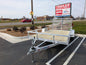White utility trailer on a paved road with a 'Trailer Sales & Parts' sign in the background.