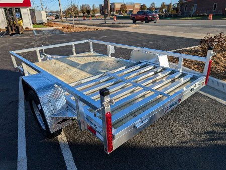 Metal utility trailer on a paved surface with a building and vehicles in the background
