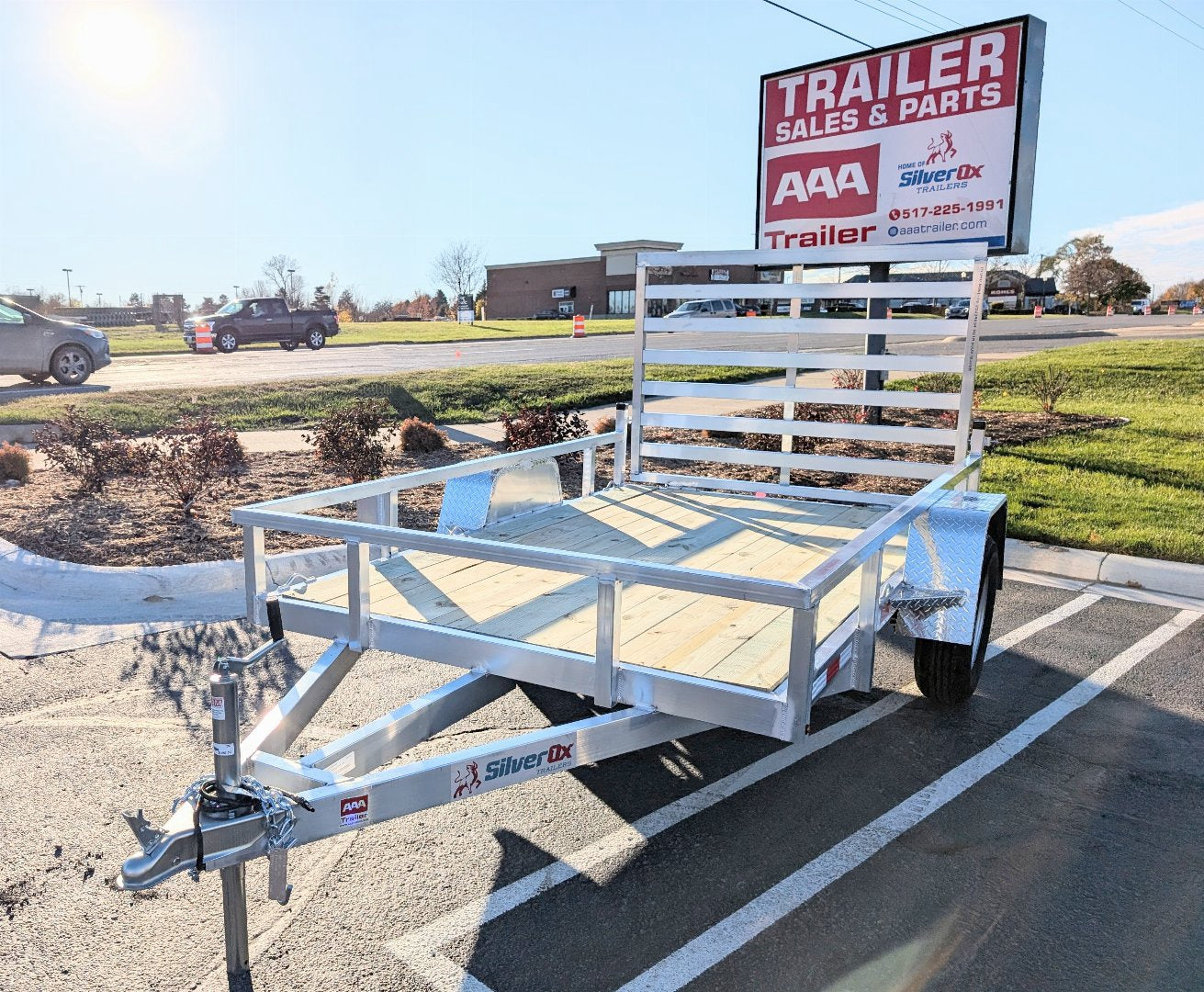 White utility trailer parked in a lot with a 'Trailer Sales & Parts' sign in the background.