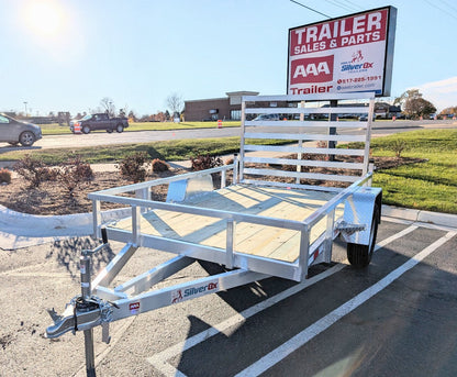 White utility trailer parked in a lot with a 'Trailer Sales & Parts' sign in the background.