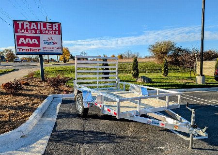 Metal trailer on a paved area with a 'Trailer Sales & Parts' sign in the background.