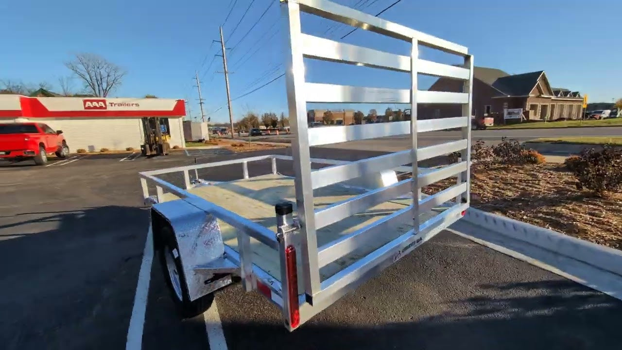 Metal trailer parked on a paved surface with a building and truck in the background