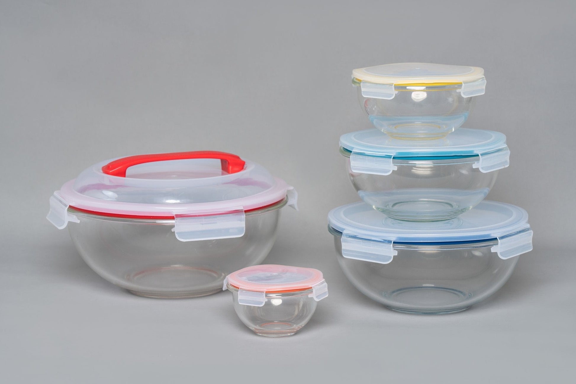 Set of glass food storage containers with colorful lids on a gray background