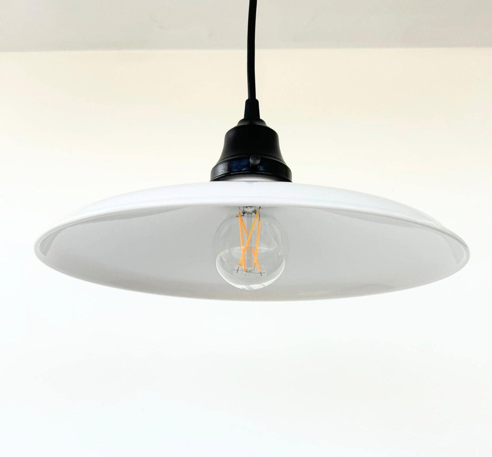 Pendant light with a white shade and visible bulb on a plain background