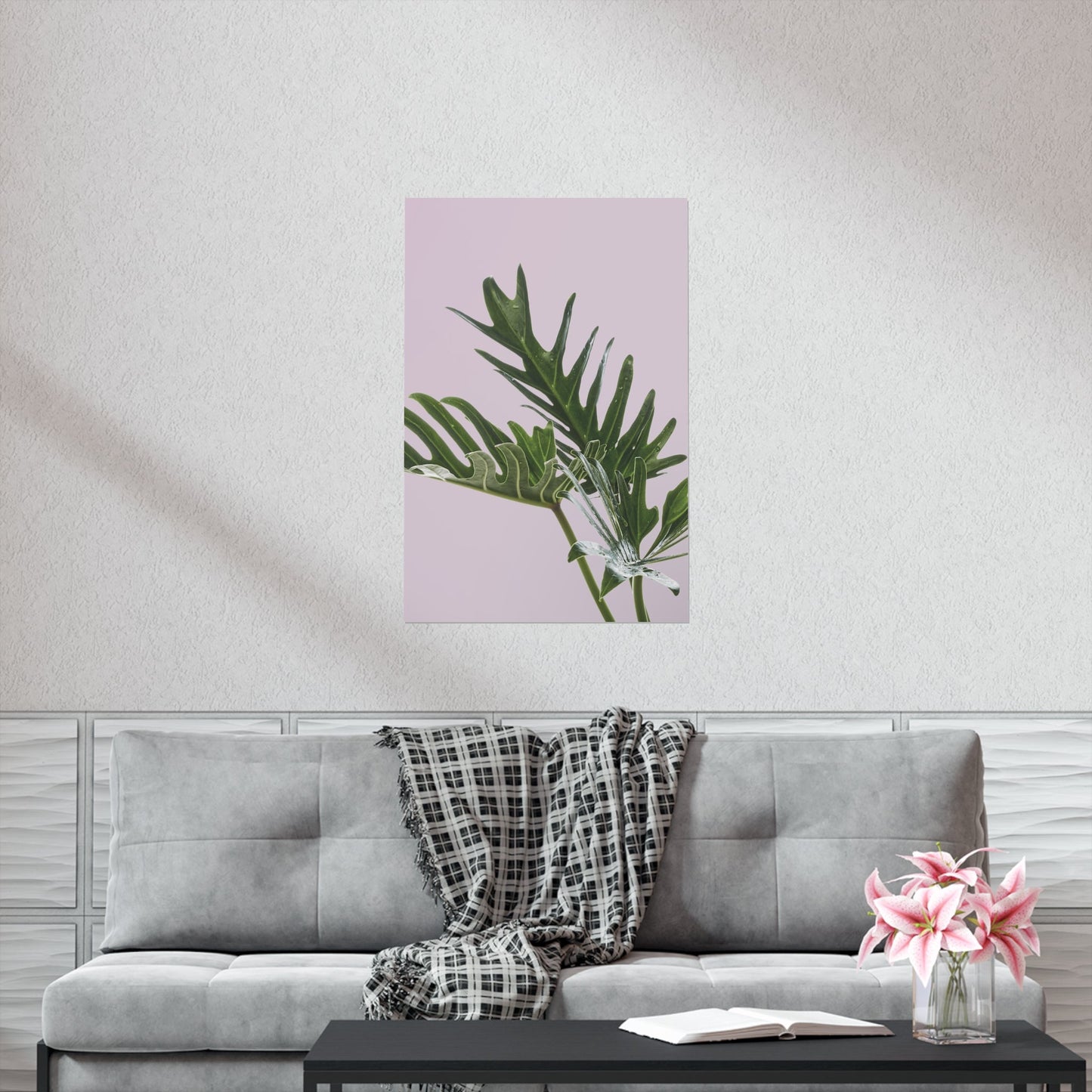 Poster of green leaves on a pink background above a gray sofa with a blanket and flowers.