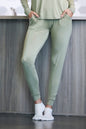 Person wearing a green tracksuit with white socks against a wooden wall.