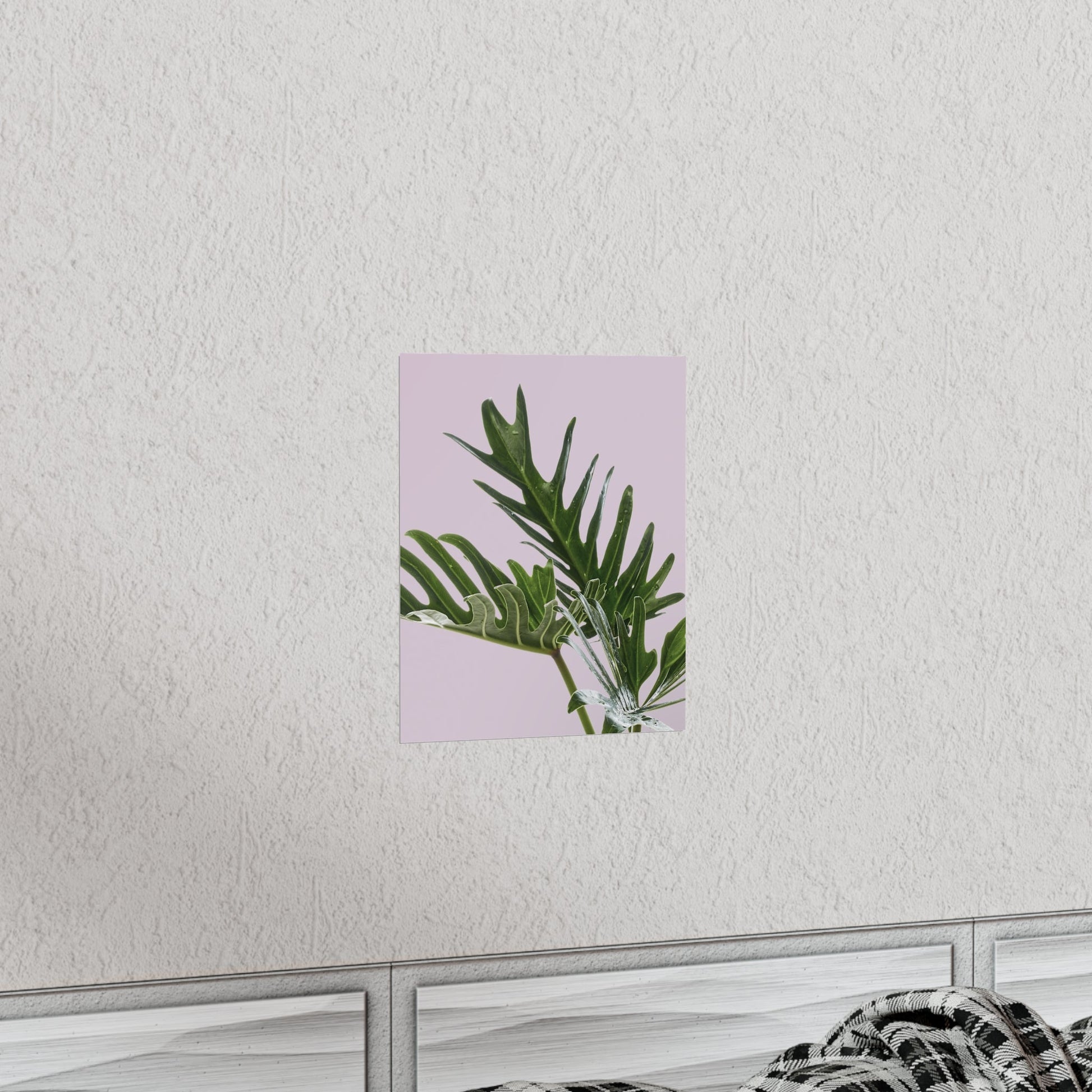 Framed artwork with green leaves on a pink background, mounted on a white wall.