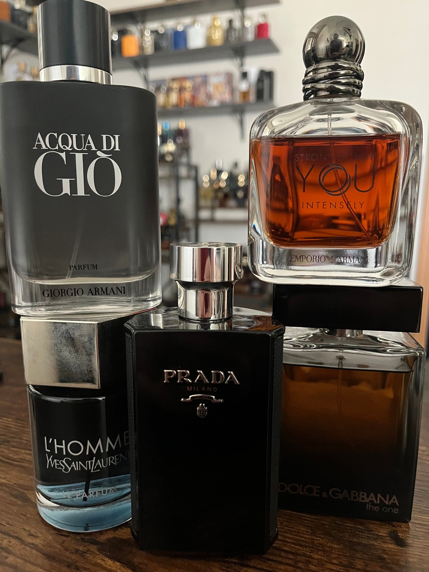 Collection of men's perfumes including Acqua di Giò, Prada, and Dolce & Gabbana on a wooden surface.