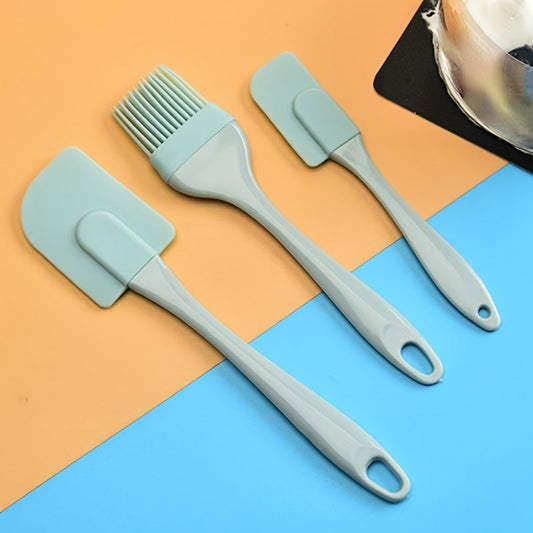 A set of three silicone kitchen utensils, including a spatula, a brush, and a scraper, in a light blue color, displayed on a two-tone background with orange and blue sections.