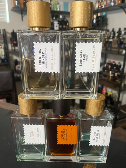 Four glass perfume bottles with wooden caps on a black surface, with a blurred background of shelves.