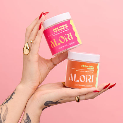 Two hands holding ALORI product containers against a pink background