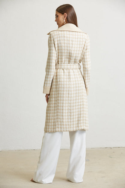 Woman wearing a checkered coat and white pants against a plain background