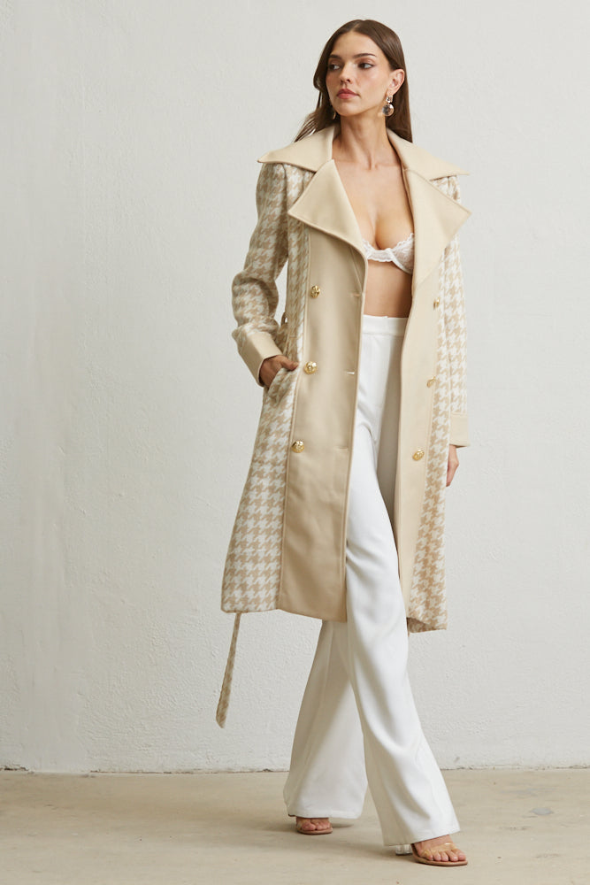 Woman wearing a long beige coat over a white outfit against a plain background