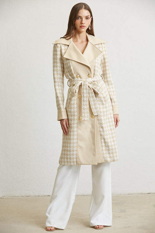 Woman wearing a beige checkered coat and white pants on a plain background