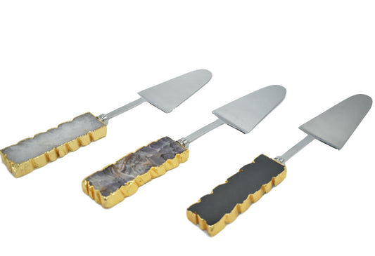 A set of three cake servers with gold trim handles and gemstone accents in amethyst, black quartz, and clear quartz.